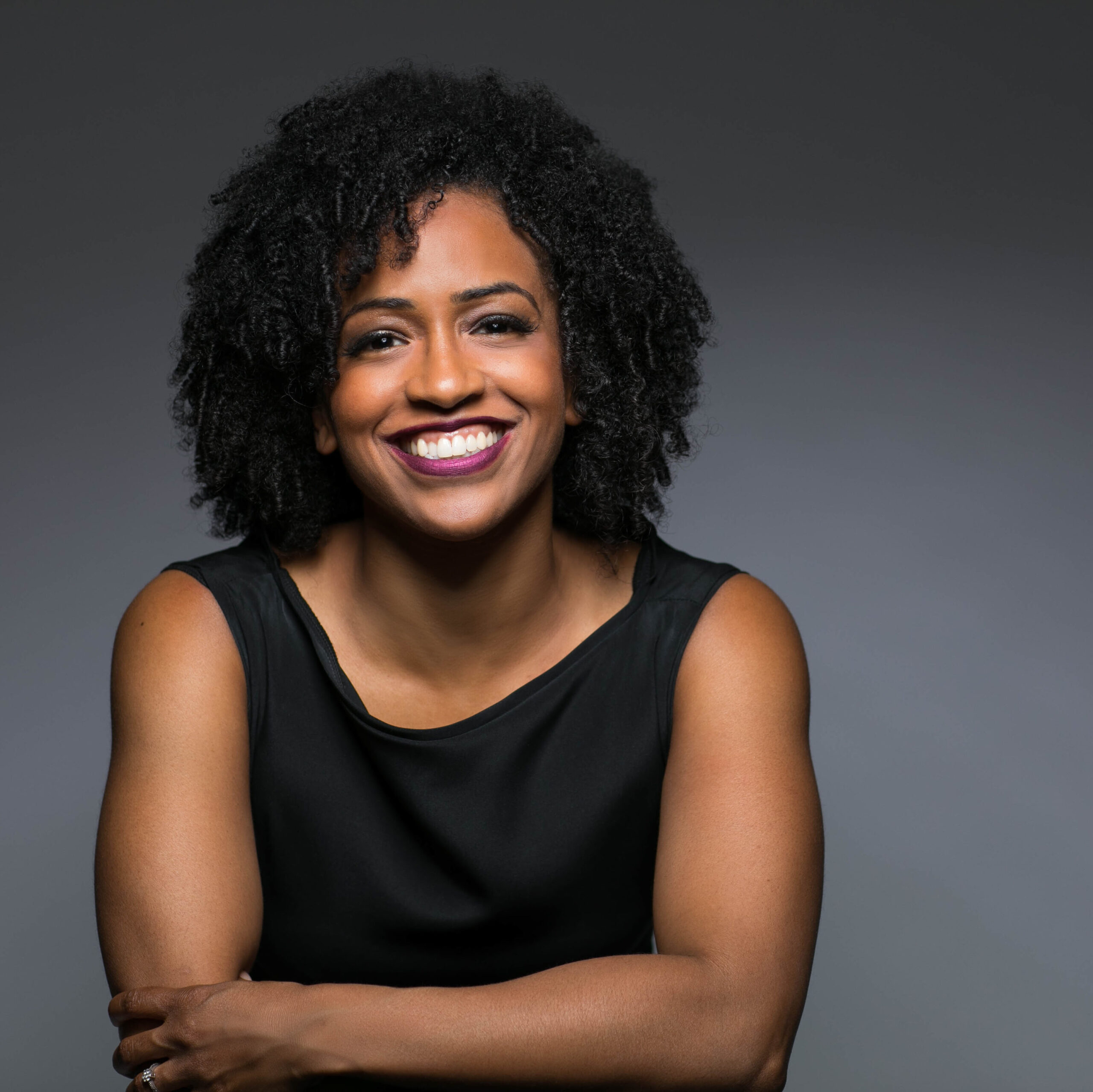 Shannon Johnson Grayson's headshot against a dark background. She has dark curly hair and is wearing a black tank 