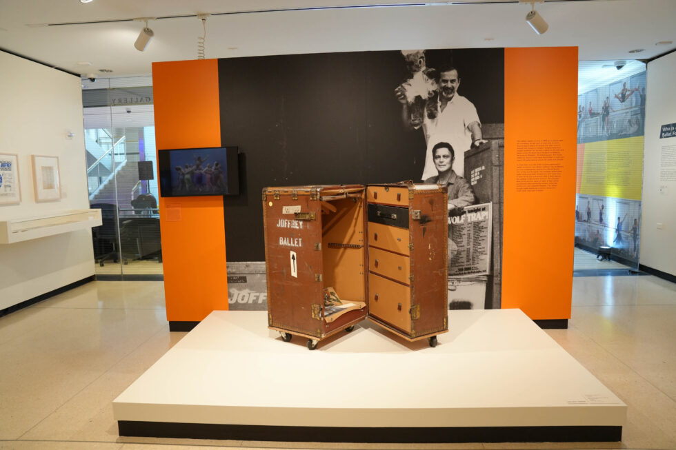 A beat-up brown trunk sits on a small white platform, half-opened to reveal its assorted contents