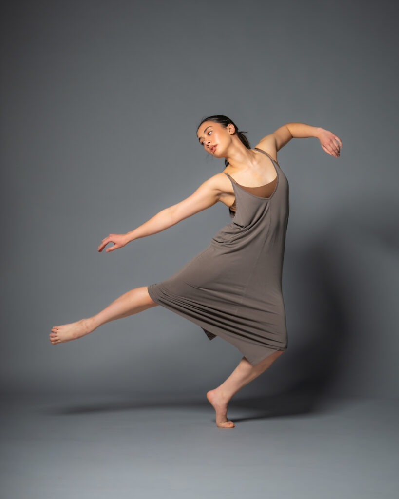 Ellie Daley dancing against a dark backdrop wearing a stretch grey dress