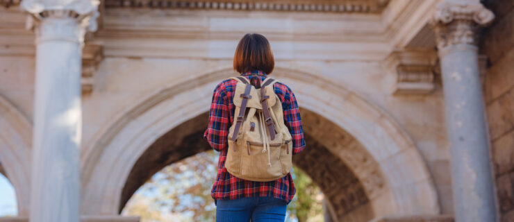 Happy asian female tourist traveller with backpack walks in old city. Woman against backdrop of Hadrian's gate - popular attraction in old city of Antalya