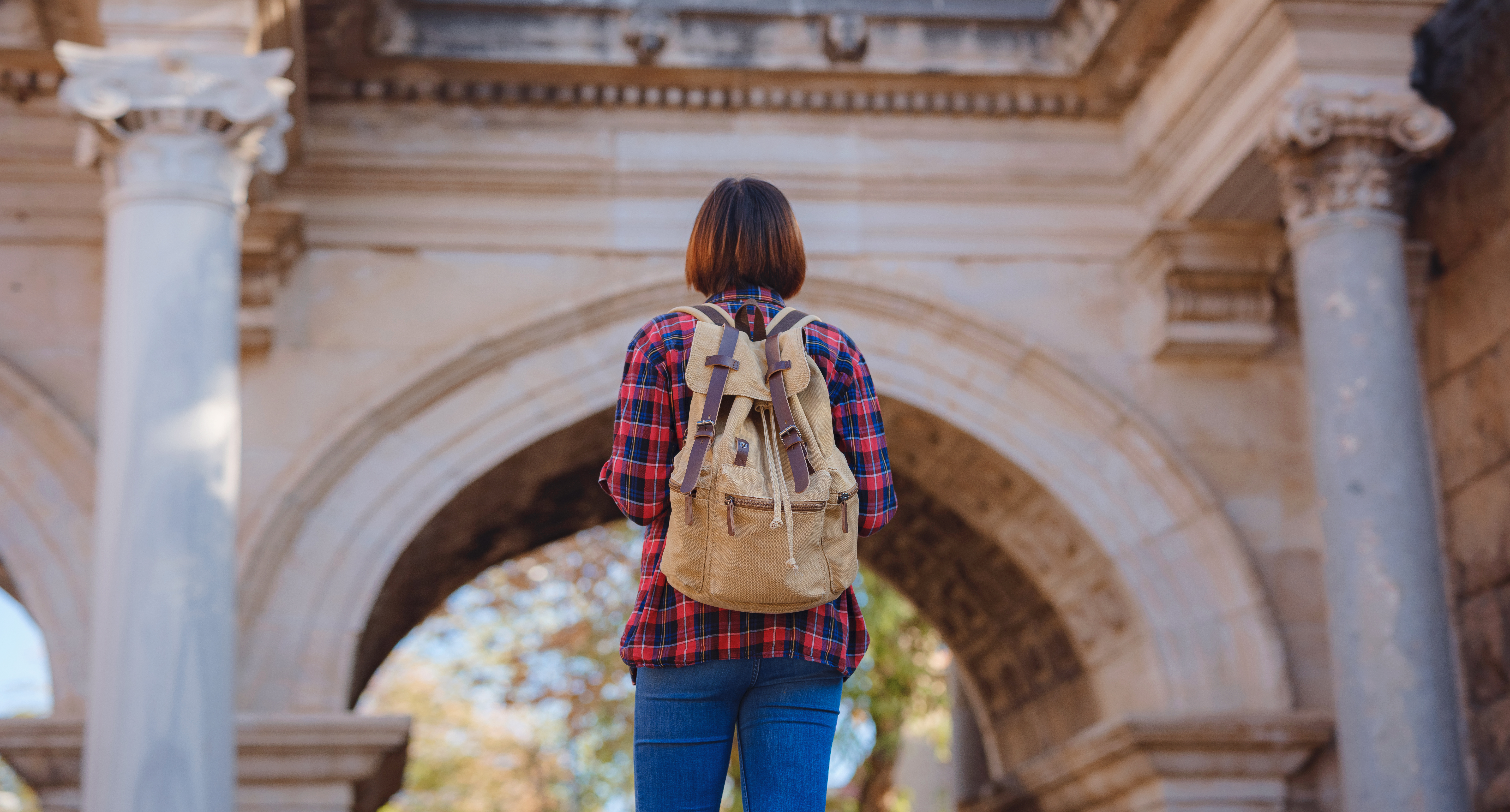 Happy asian female tourist traveller with backpack walks in old city. Woman against backdrop of Hadrian's gate - popular attraction in old city of Antalya