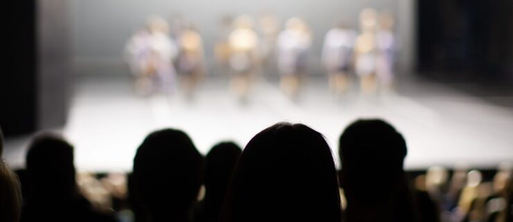 a group of people huddled together watching a dance performance on stage