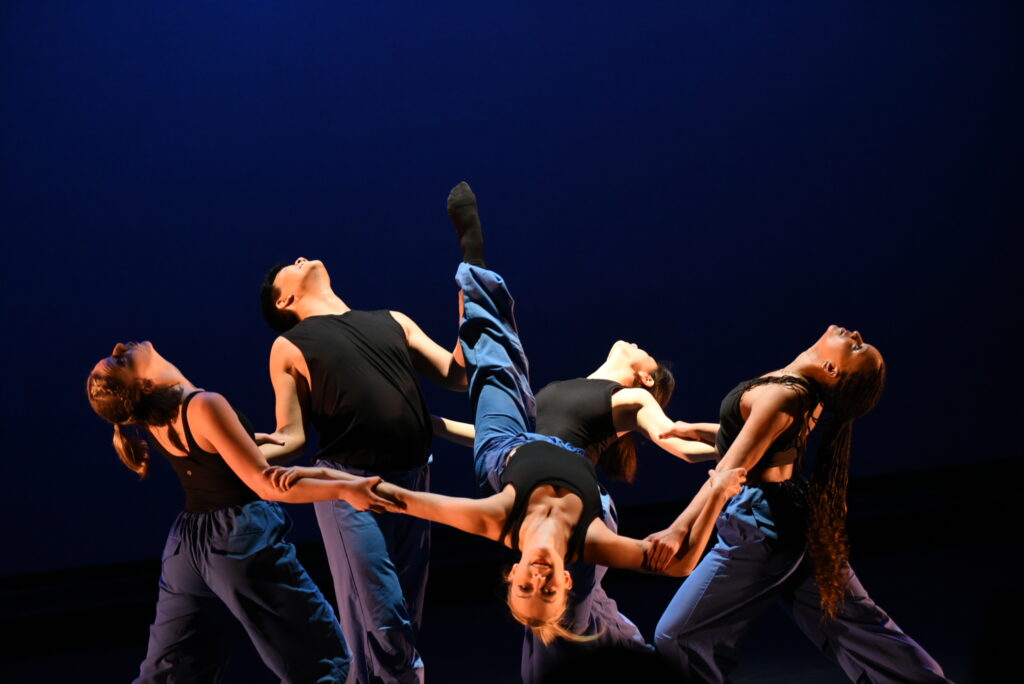 a female dancer lifted upside down in an arch back while being supported by four other dancers