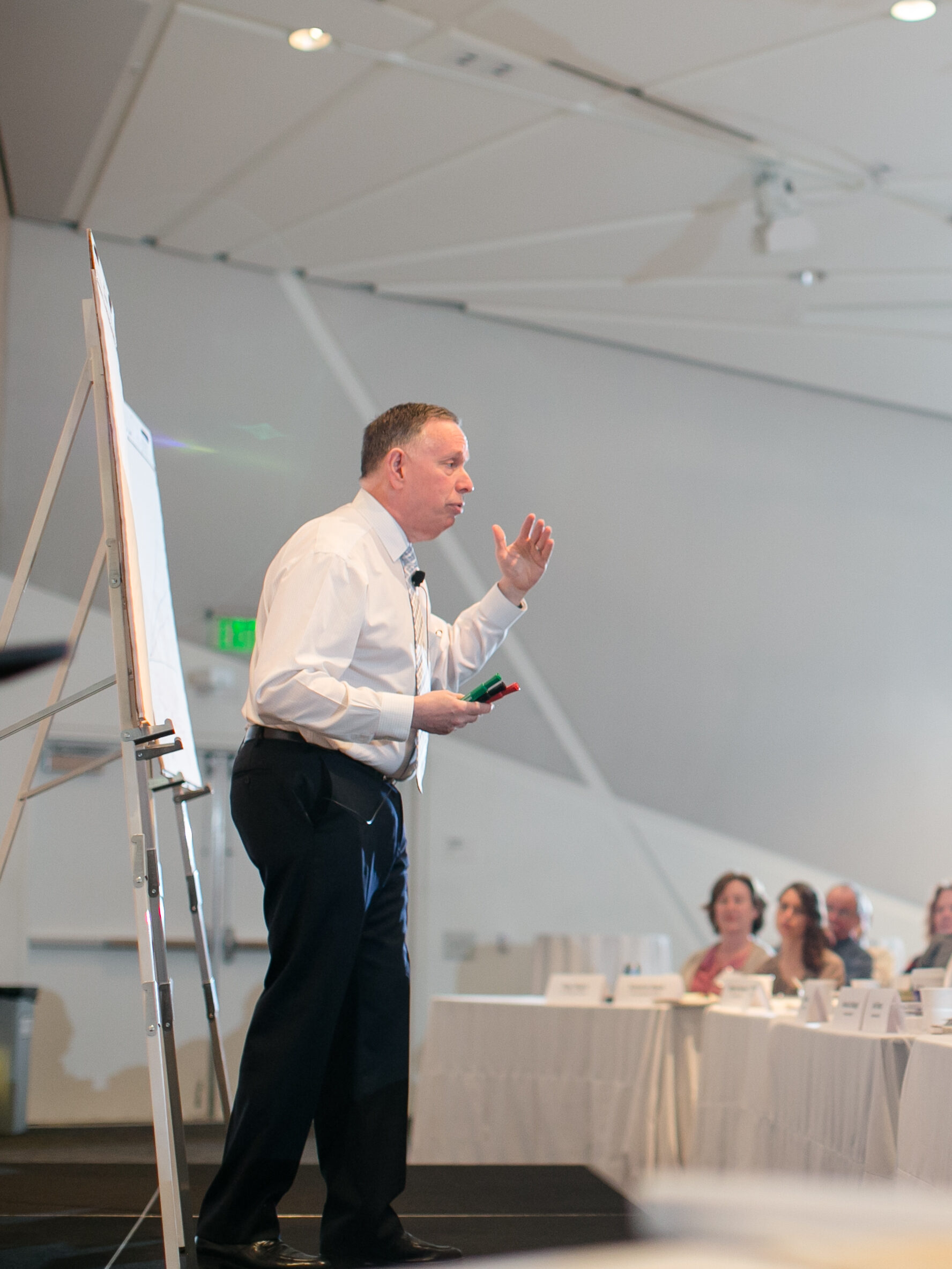 a man giving a presentation to people sitting at tables 