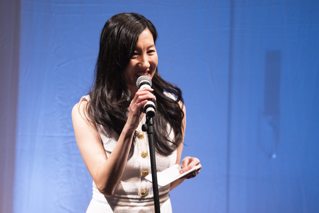 a woman speaking into a microphone while holding notes 