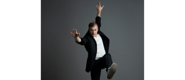 a male dancer wearing street clothes and sneaker posing in front of a grey backdrop