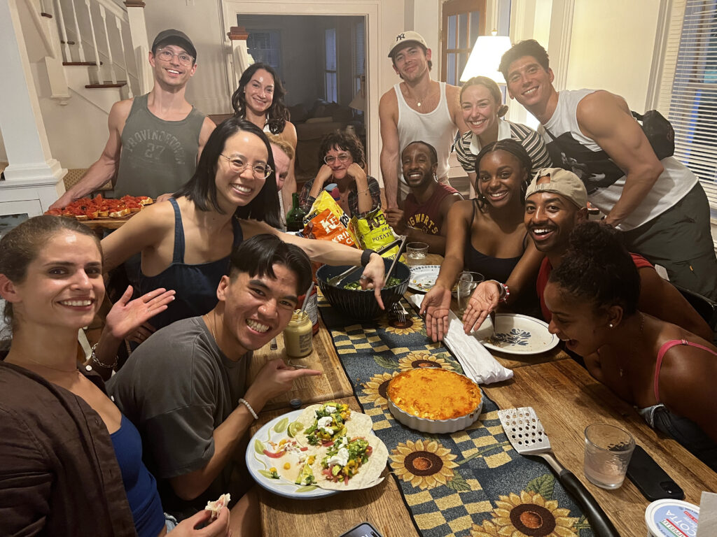 A large group of dancers huddled around a table pointing to the center where the dip is placed 