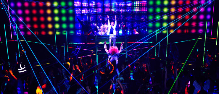 An overhead shot of a large crowd on a dance floor illuminated with streaks and orbs of trippy rainbow-hued lights