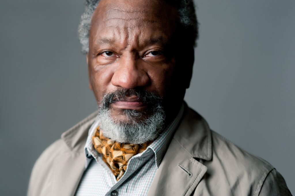 Donald Byrd's headshot. A Black man with grey hair and beard, wearing a collared shirt and tan jacket.