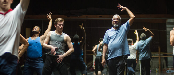 Donald Byrd directing dancers in the studio. He lifts his arm above his head to match the dancers' movement