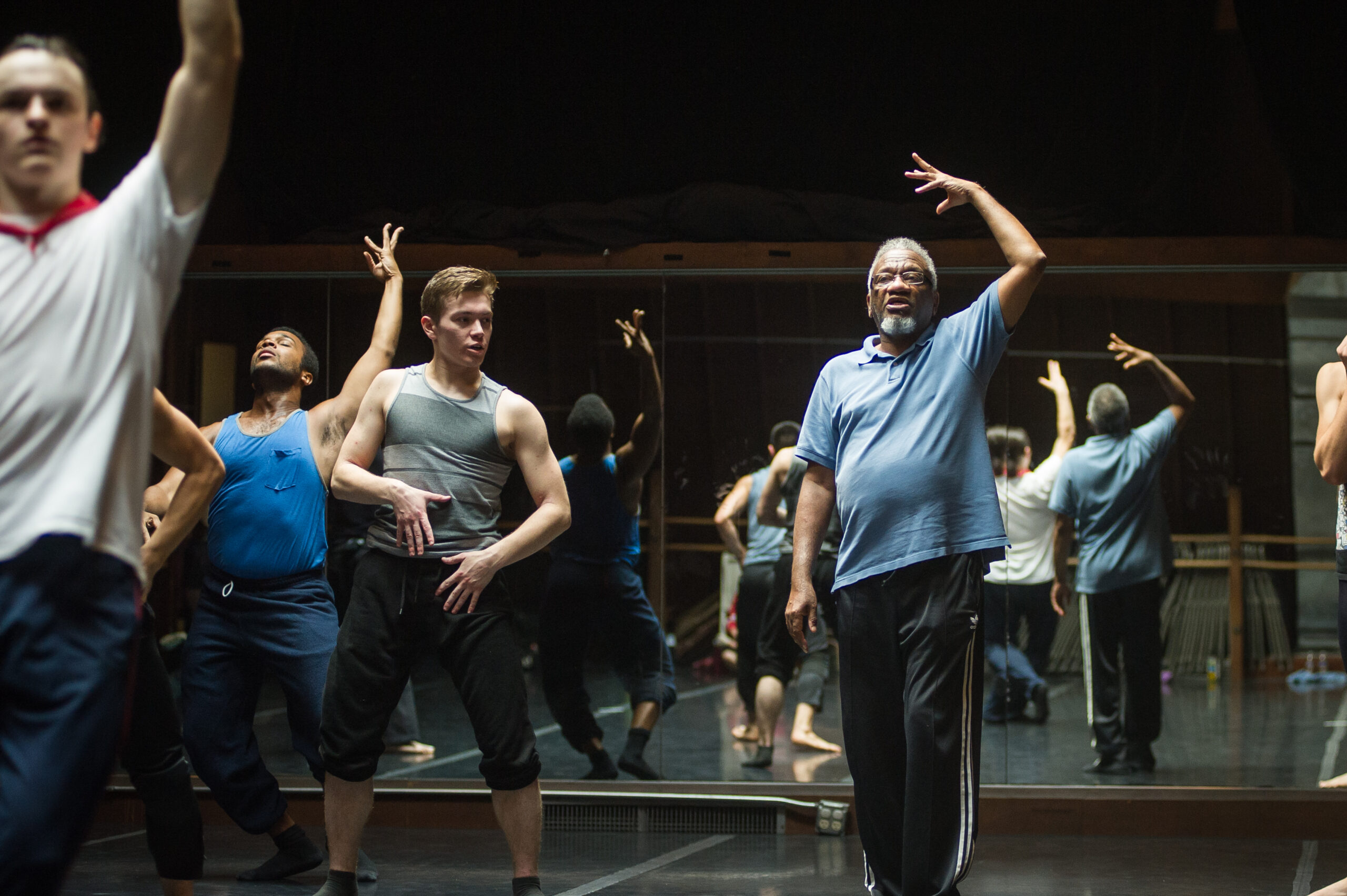 Donald Byrd directing dancers in the studio. He lifts his arm above his head to match the dancers' movement