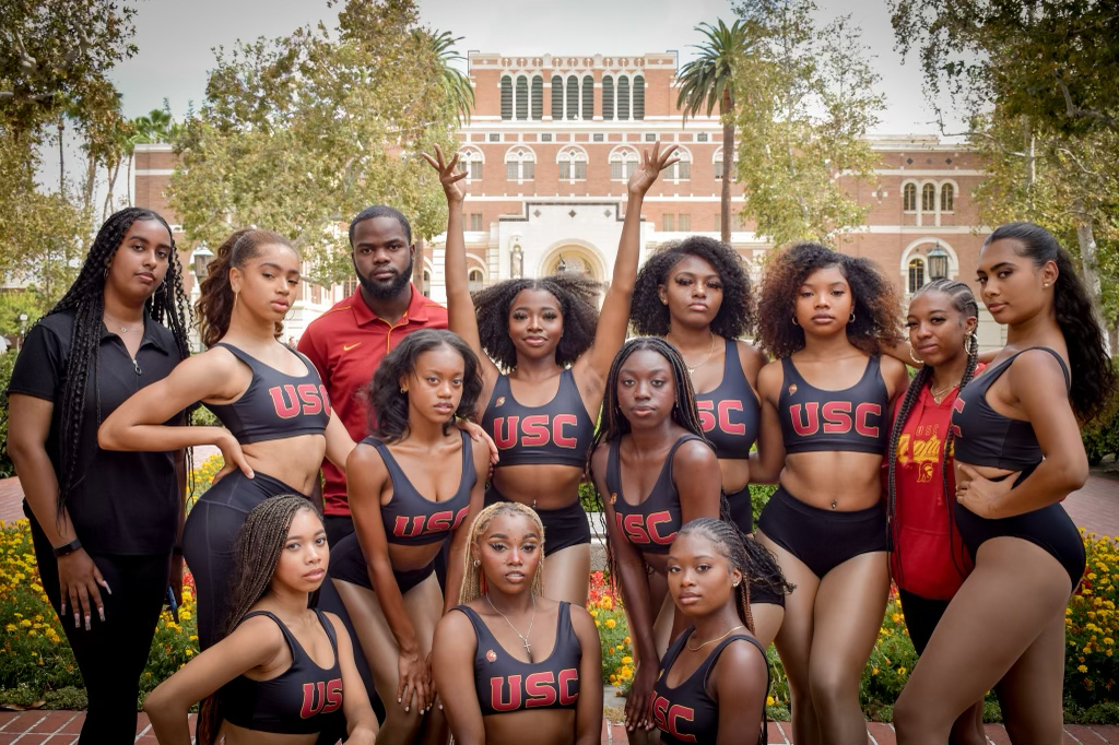 A group of dancers wearing USC uniforms. One dancer extends her arms overhead 