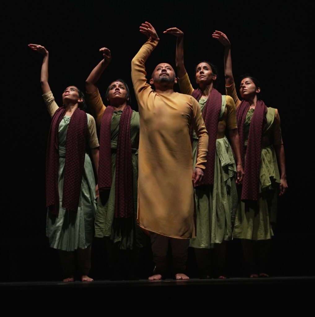 Akram Khan stands at the point of a v, two women on either side of him. All raise a sinuously curving hand overhead, eyes turned up.