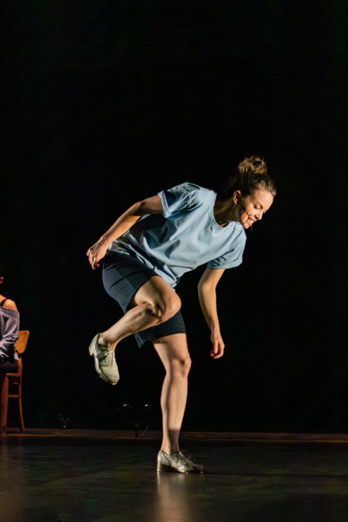 Michelle Dorrance tapping on stage wearing a blue t-shirt.