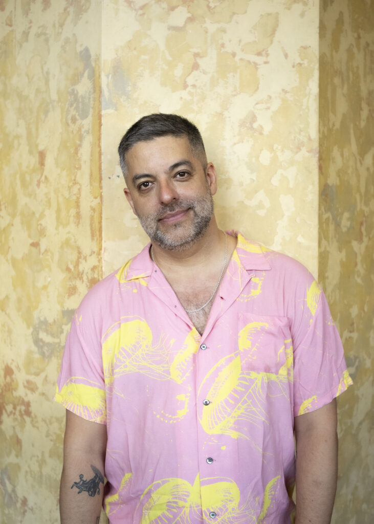 Miguel Gutierrez's headshot. A man wearing a pink and yellow polo shirt.