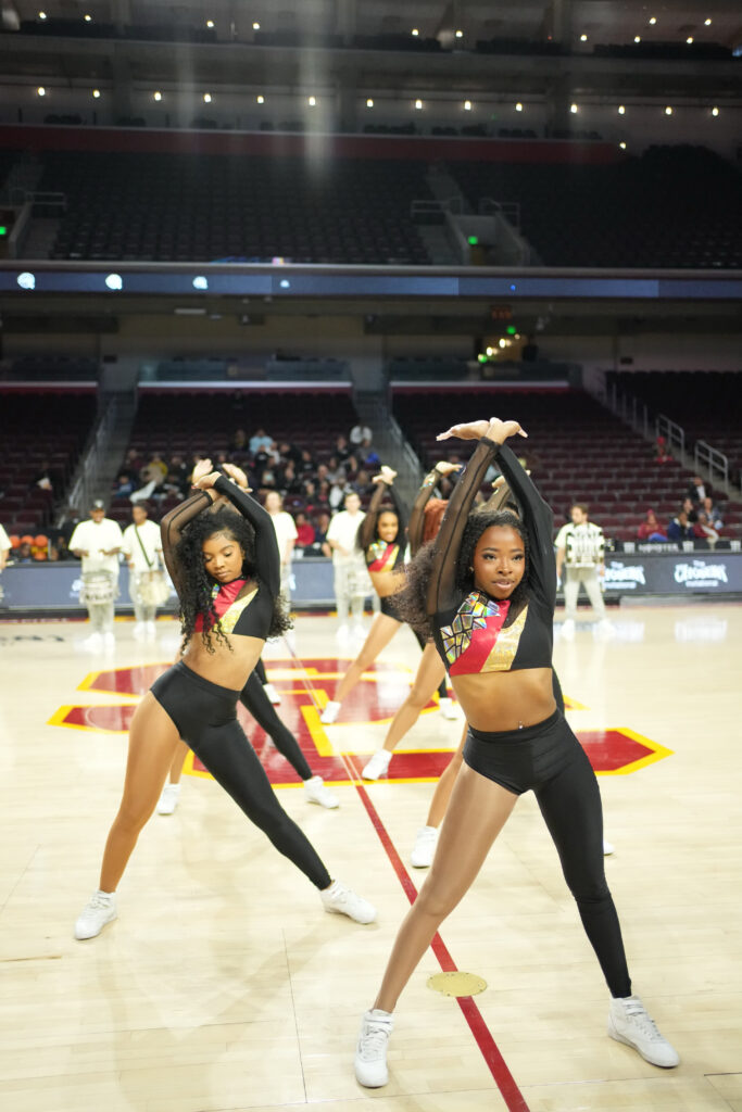 dancers performing on a basketball court wearing long sleeve cropped shirts and one-legged pants 