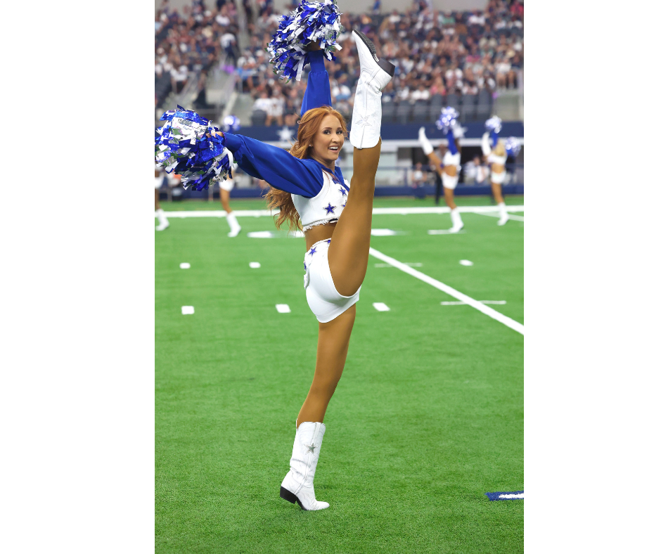 Charly Barby high kicking on the field wearing a blue and white uniform while holding poms