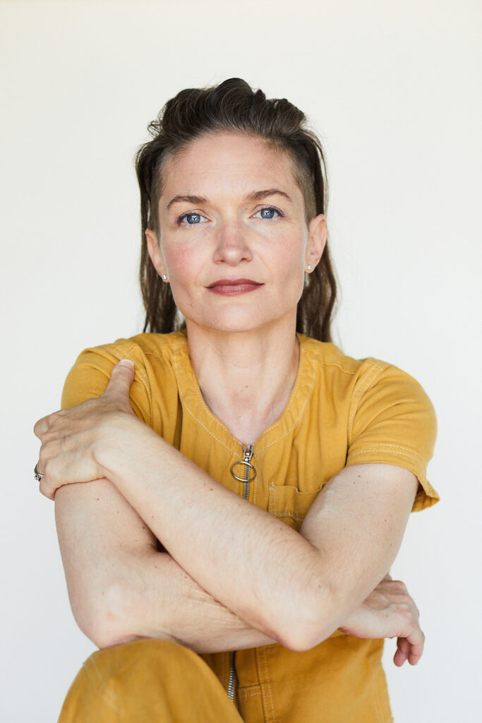 Banning Bouldin's headshot. She's wearing a yellow jumpsuit and sitting with her arms crossed against a white backdrop. 