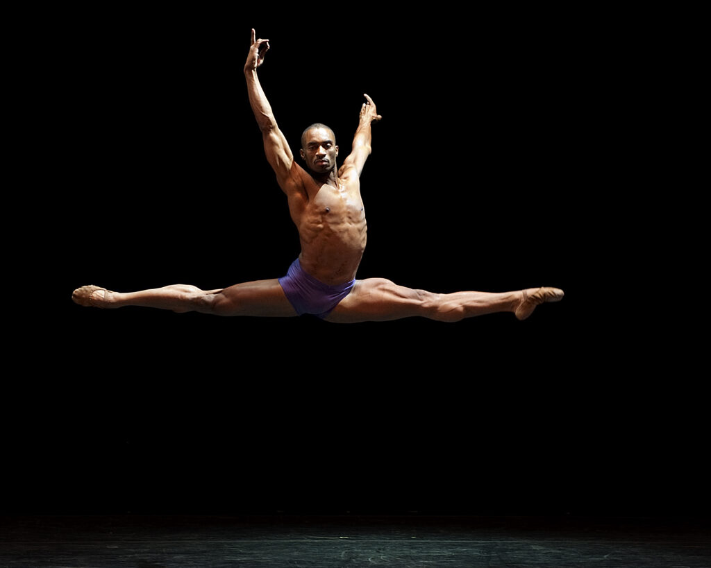 Desmond Richardson performing a grand jete on stage 