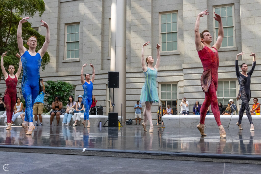 Moveius Contemporary Ballet dancers in 4th position with their arms raised above in 5th. They perform outside in front of the National Portrait Gallery 