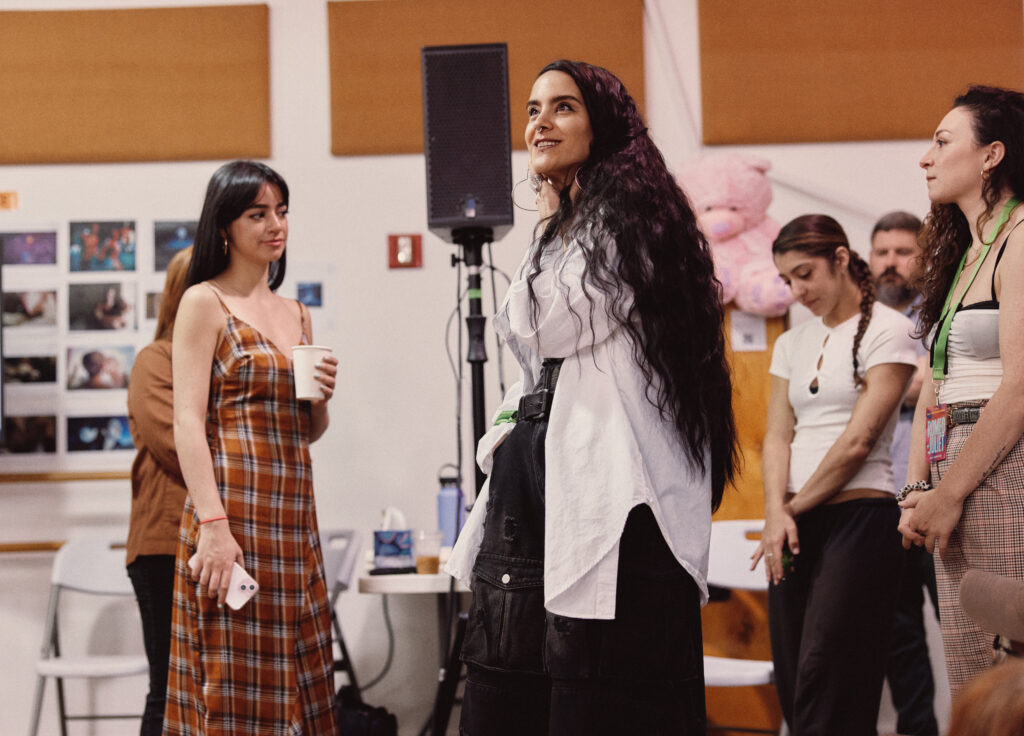 Sonya Tayeh smiling and looking upwards while standing next to actors and staff in a rehearsal room