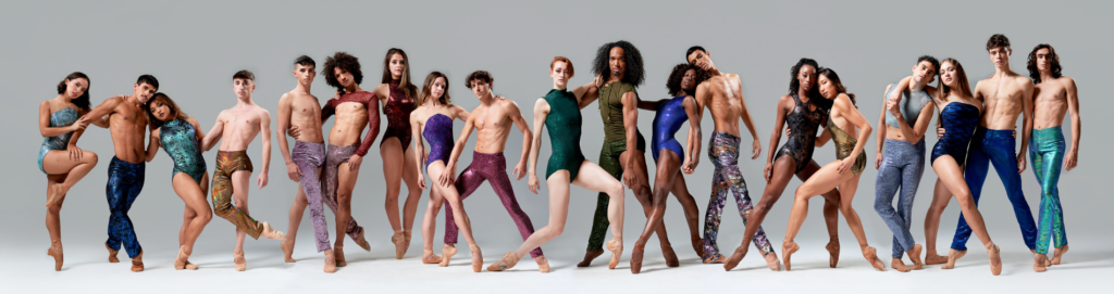 A large group of dancer in various poses against a grey backdrop 