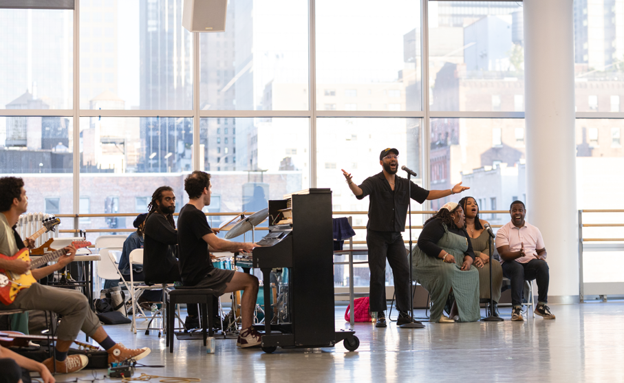 Du’Bois A’Keen sining into a mic in Ailey studios with backup musicians and singers.