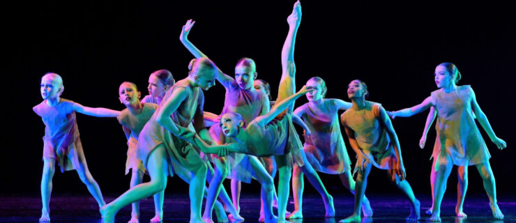 A group of young students on stage forming a tableau with a variety of poses.