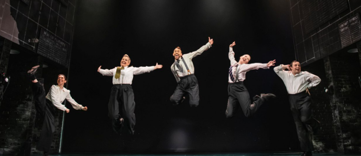 5 dancers jumping in the air on stage while wearing white button downs, ties, and suspenders