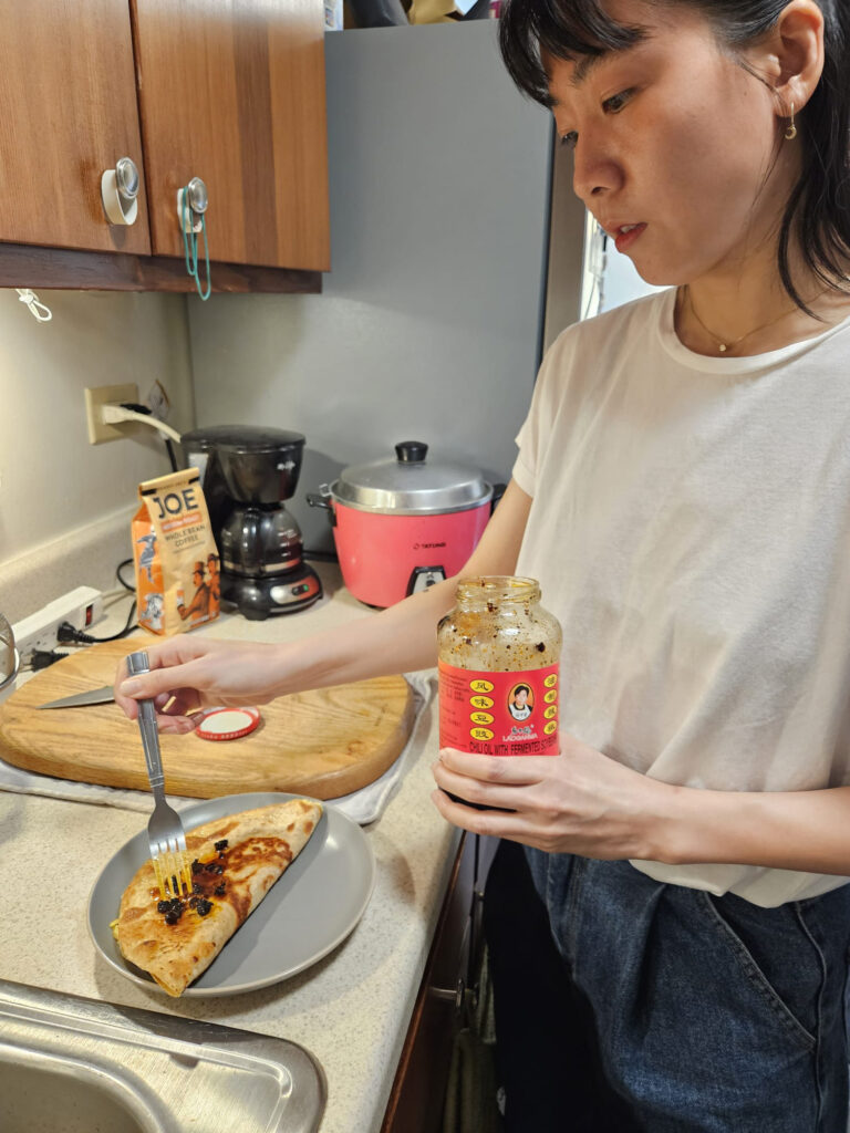 A woman cooking in her kitchen. She spreads sauce on a prepared omelet. 