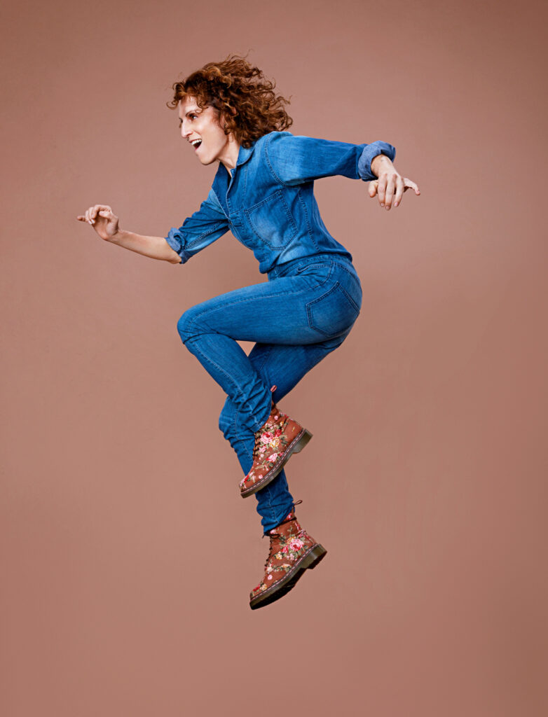 Nancy Dobbs Owen wearing an all jean outfit and floral combat boots. She jumps in the air with her legs slightly bent.