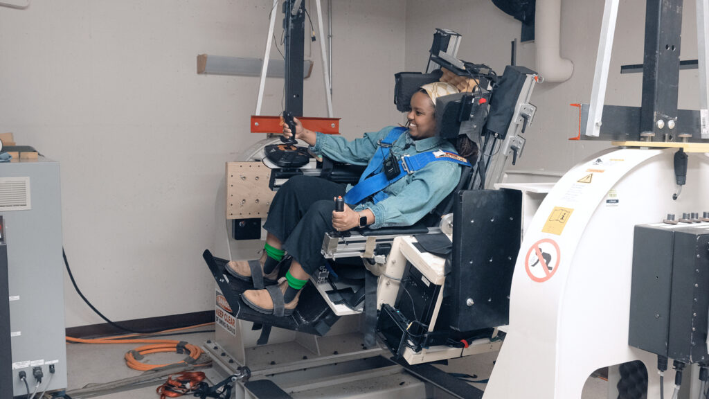A dancer sitting in a large chair with numerous controls. 