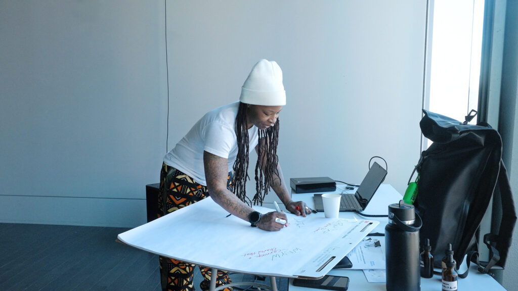 Sage Ni’Ja Whitson writing on a large notepad at a desk. 