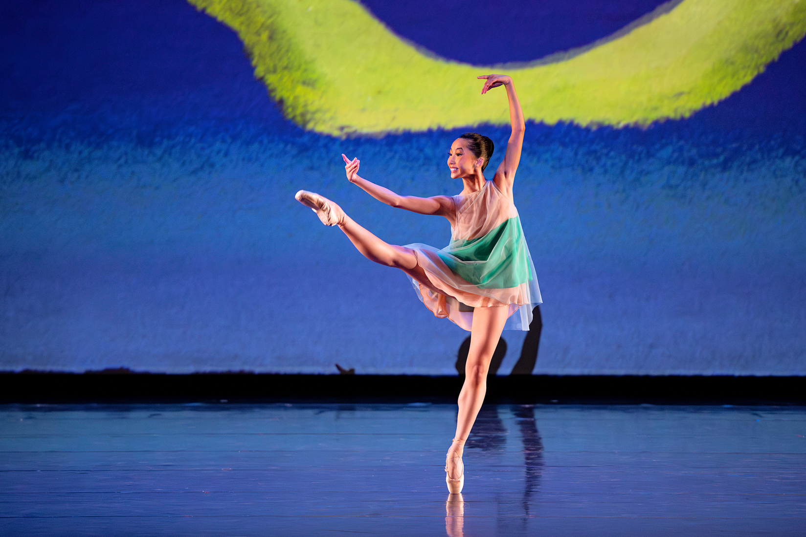 Lexi McCloud balances en pointe with her right leg extended front and her arms in 4th position. She wears a loose tulle dress with a green stripe.