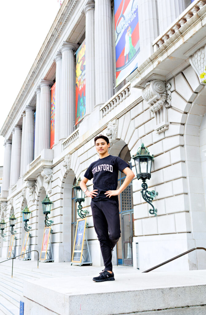 Lleyton Ho standing in front of a stone building. He wears a Stanford t-shirt, black pants, and sneakers.