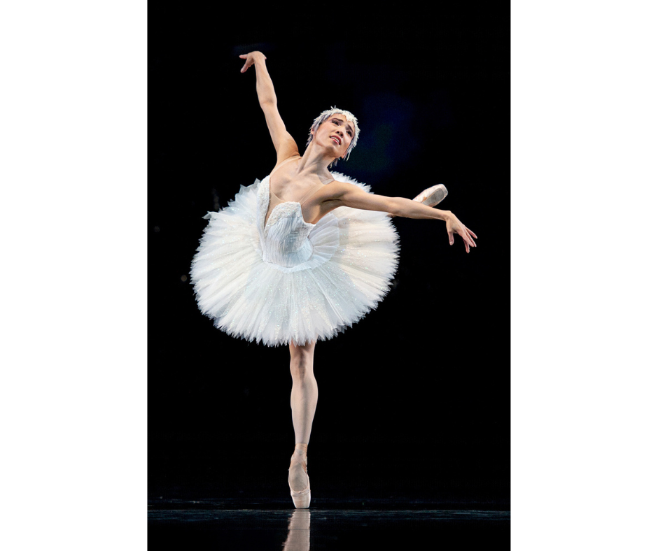 Frances Chung in Swan Lake. She wears a white tutu and head piece. She performs an attitude derrière on stage.