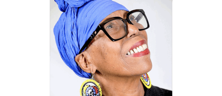 Lula Washington's headshot. She wears a purple head scarf, large glasses, and colorful earrings.