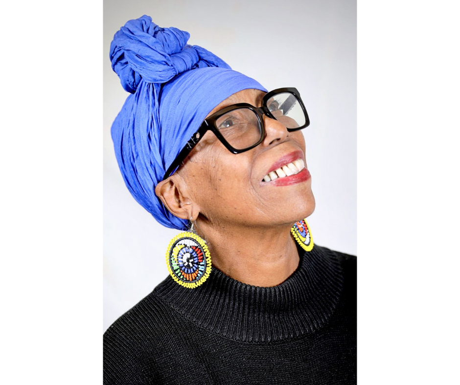 Lula Washington's headshot. She wears a purple head scarf, large glasses, and colorful earrings.