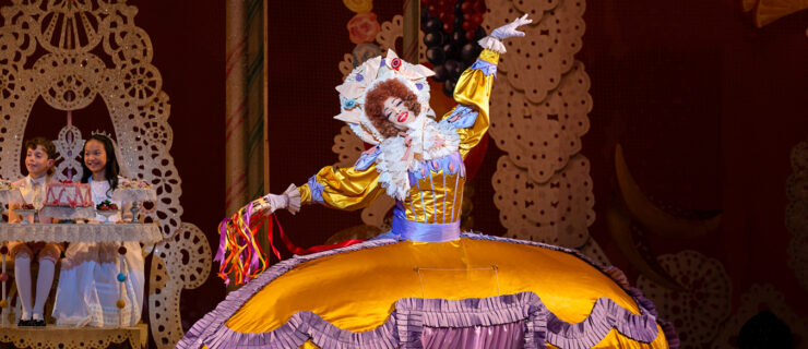Gilbert Bolden III as Mother Ginger. He wears an orange and purple dress with a large hoop skirt. He has a frilly bonnet and holds a tambourine.
