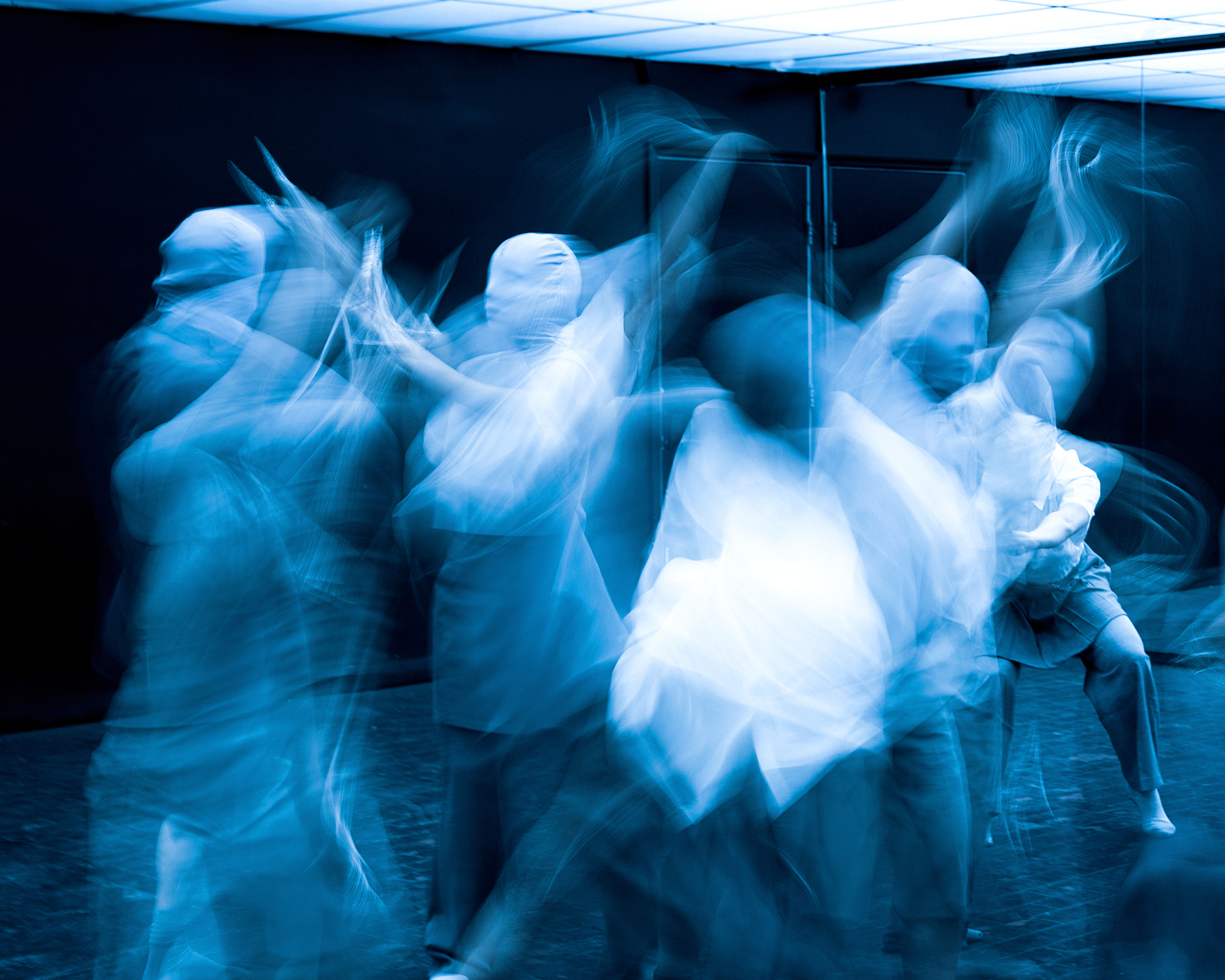 A blurry photo of Sun Kim Dance Theatre. Multiple dancers reach and twist their bodies around each other.
