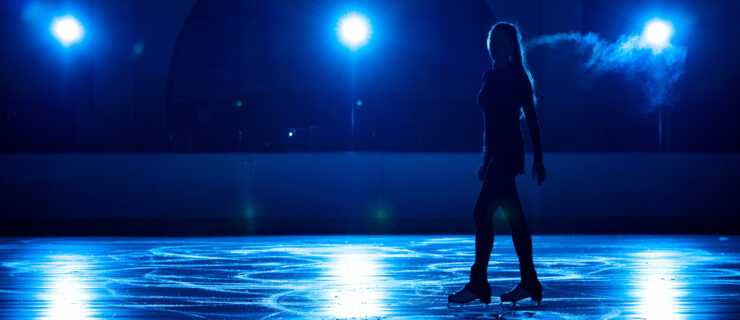 A lone figure skater is pictured in silhouette on the ice, bathed in blue lights.