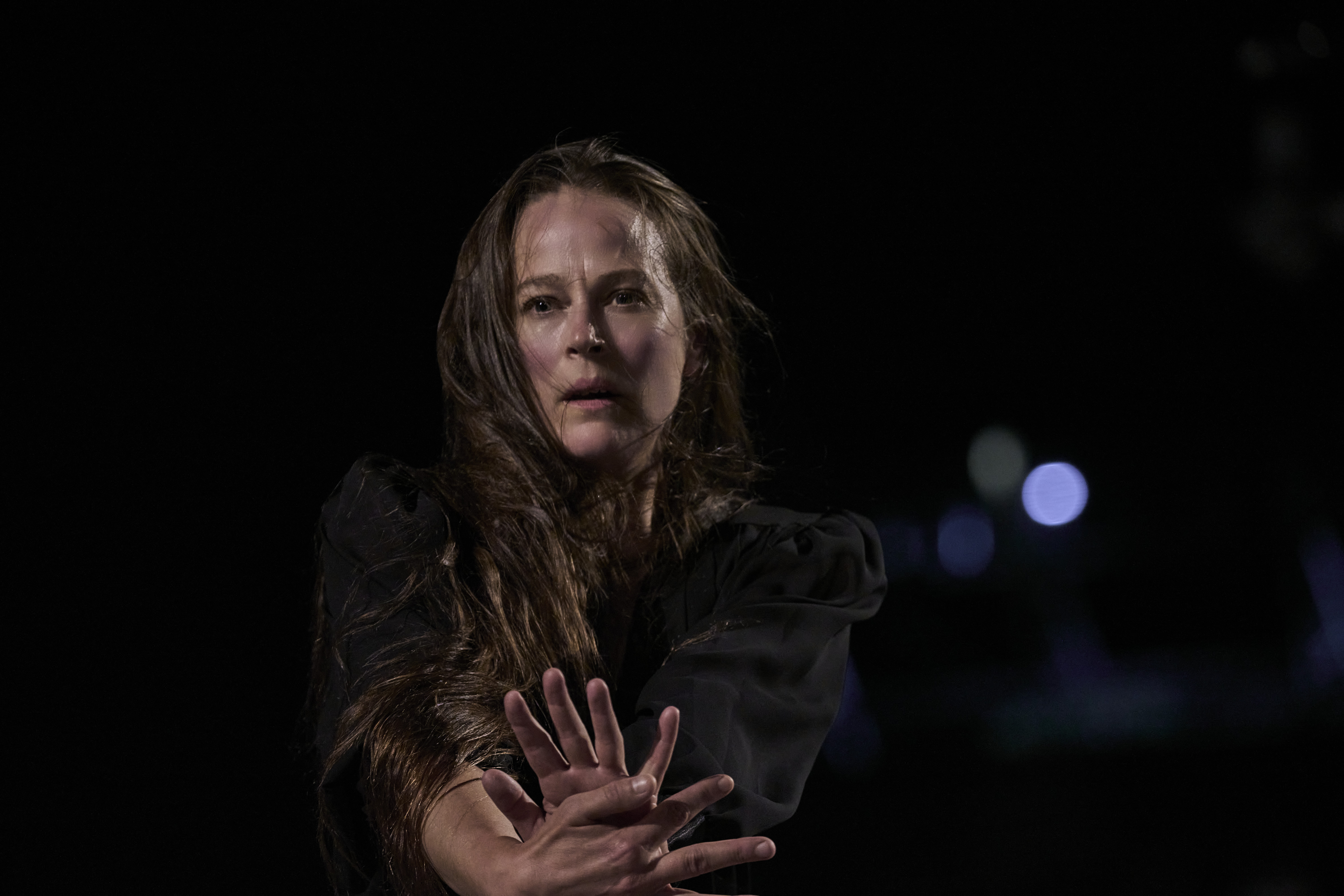 Bobbi Jene Smith stares intently forward, long hair flying in the wind around her face. She presses her arms forward, palm to palm.