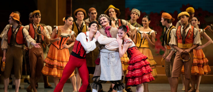 Caniparoli—costumed as Don Quixote in breeches, a neck scarf and a curled mustache—stands onstage at the center of a crowd, his arms crossed, smiling slightly. The dancers playing Basilio and Kitri hang adoringly on his arms.