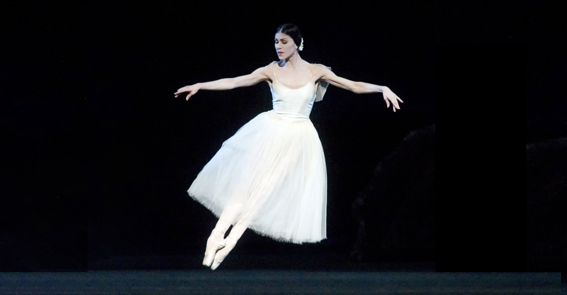 Herrera performs an assemble on stage while wearing a white romantic tutu.
