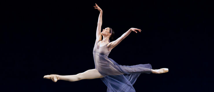 Ava Sautter performs a saut de chat on stage. She wears a flowy purple mesh dress.