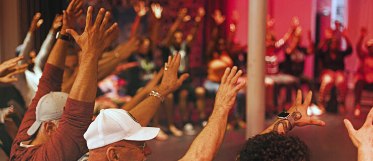 Workshop participants of Recovery in Motion sit in a circle and lift their hands overhead.