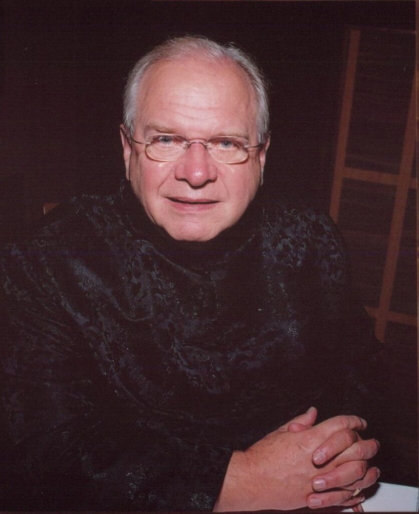 Stevenson, wearing a black shirt and glasses, looks directly into the camera, half-smiling.