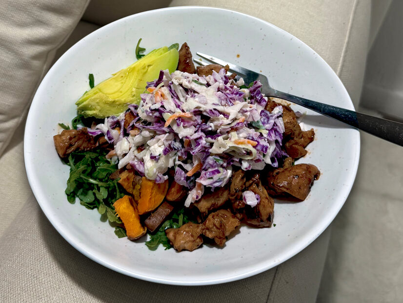 Sweet potatoes, BBQ chicken, coleslaw, avocado, and arugula on a white plate. 