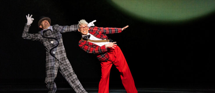 Brandon “Private” Freeman, wearing a grey plaid suit, and Christian Squires, wearing a red plaid jacket and pants, lean to the right while smiling on stage.