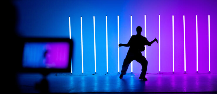 Camcorder display and blurred frame with young guy dancing street dance hip hop in a studio with neon lighting tube on a colorful background